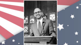 A photo of a man at a podium in front of an american flag.