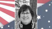 A photo of a woman with glasses and an american flag background.