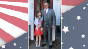 A man and a girl standing in front of an american flag.