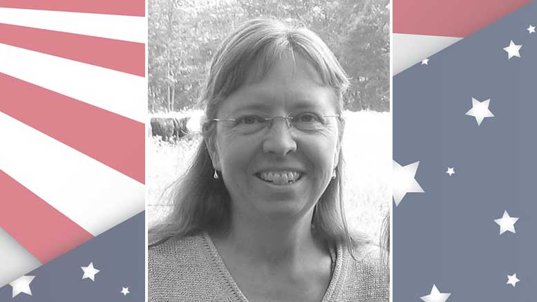 A photo of a woman with glasses in front of an american flag.