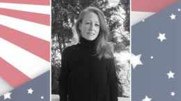 A black and white photo of a woman in front of an american flag.