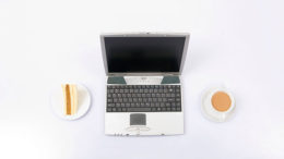 A laptop computer with a cup of coffee and a piece of cake.