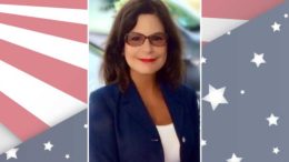 A woman in glasses is standing in front of an american flag.