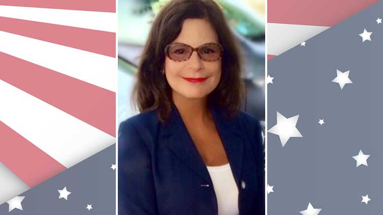 A woman in glasses is standing in front of an american flag.