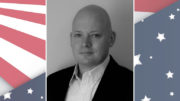 A photo of a bald man in front of an american flag.