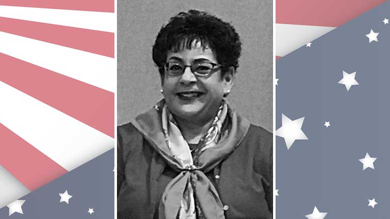 A photo of a woman with glasses in front of an american flag.