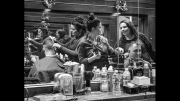 A black and white photo of people getting their hair done in a barber shop.