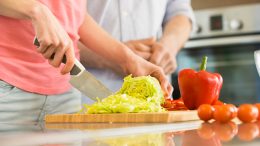 Two people chopping vegetables on a cutting board.