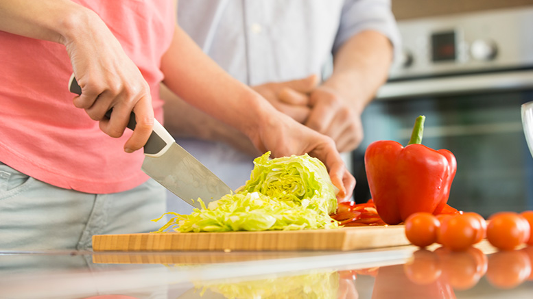 Two people chopping vegetables on a cutting board.