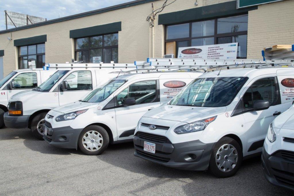 A row of white vans parked in front of a building, showcasing Capital Construction's expertise in James Hardie siding installations for various projects.