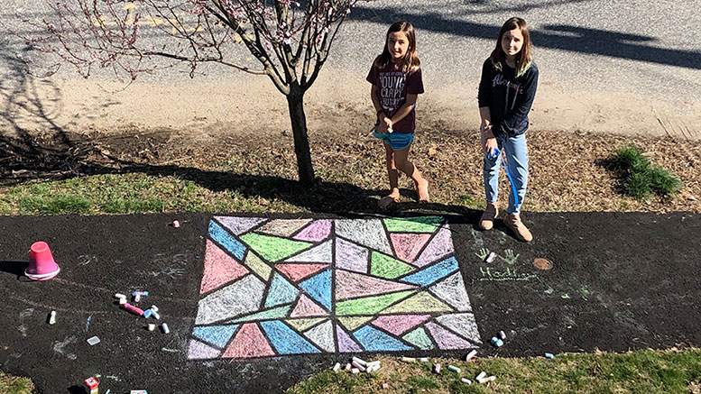 Two girls from Milton sharing their spring artwork as they stand next to a chalk drawing on the sidewalk.
