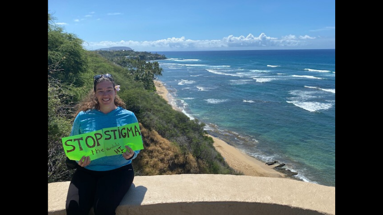 A woman holding a sign that says stop joins the Stop the Stigma Virtual 5K event, which successfully raises $65,000 for Mental Health.