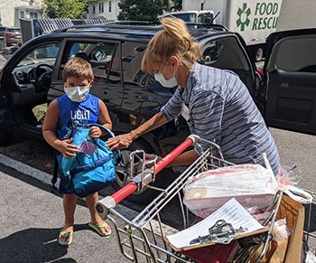 Interfaith Social Services volunteer Marzie Gans, of Quincy, (right) gives a backpack to Joshua Hashorva, of Braintree (left). Volunteers distributed more than 600 backpacks to the children of Interfaith’s food pantry clients in August.