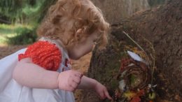 A little girl playing with a fairy house in the Eustis Estate woods.