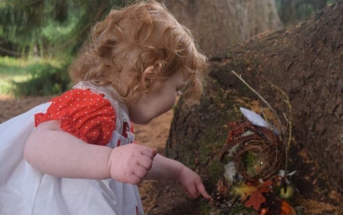 A little girl playing with a fairy house in the Eustis Estate woods.