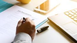 A person writing a resume on a desk with a laptop, ensuring the right processes for finding qualified candidates.