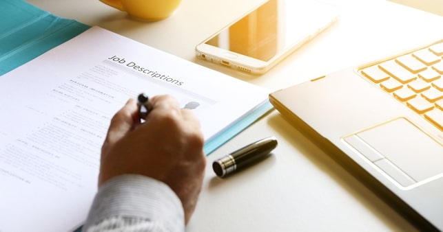 A person writing a resume on a desk with a laptop, ensuring the right processes for finding qualified candidates.