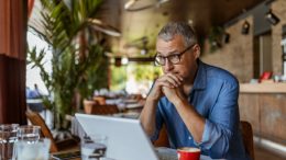 A man sitting in a restaurant looking at his laptop, while realizing that the time to recession-proof his business is now.