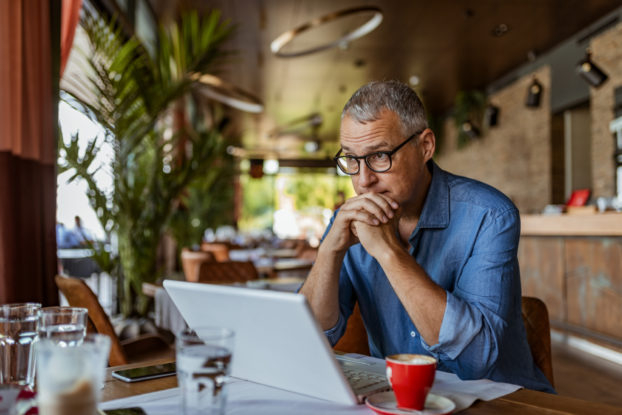 A man sitting in a restaurant looking at his laptop, while realizing that the time to recession-proof his business is now.