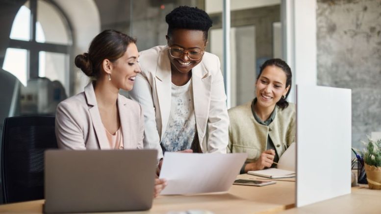 Three business women working collaboratively with a laptop in an office.