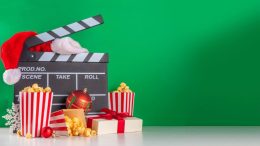 A movie clapper board with popcorn and santa hat on a holiday background.