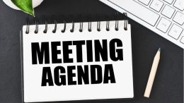 A notebook with the word meeting agenda next to a keyboard.