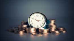 A clock symbolizing business success sitting on a pile of coins.