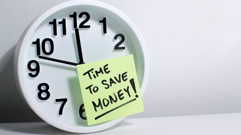 A clock with a sticky note saying the time to save money for business success.