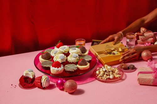 Edible Arrangements - A woman is carefully arranging Valentine's Day cupcakes on a pink table.