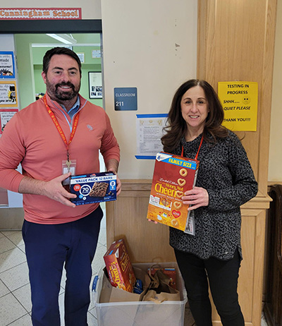 Two people standing in a hallway during Ramadan in Milton 2024, holding boxes of cereal and reflecting on devotion to the community.