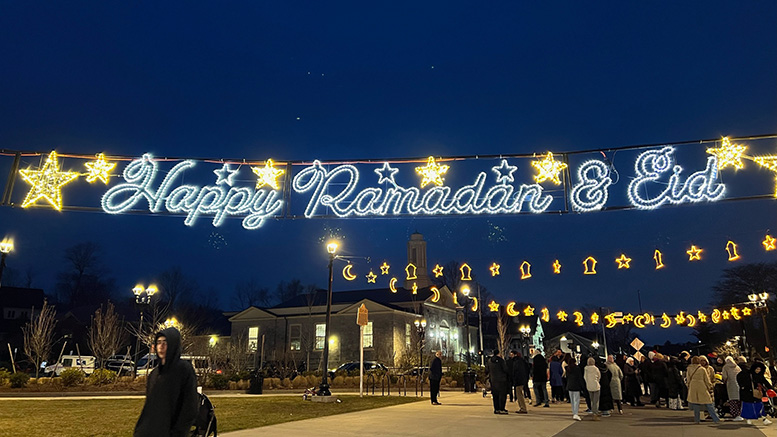 Celebratory lights spelling "happy Ramadan & eid" above a crowd gathered at dusk, embodying devotion and community during Ramadan 2024: A time for reflection.