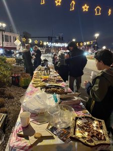 Community members gather around a table of shared food at a Ramadan 2024 night-time outdoor event, demonstrating devotion and community.
