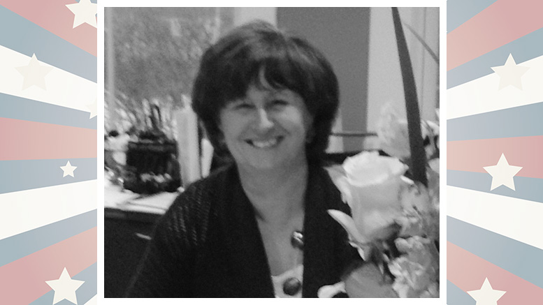 A smiling woman seated at a table with a bouquet of white roses, framed by a border with red, white, and blue stars and stripes.