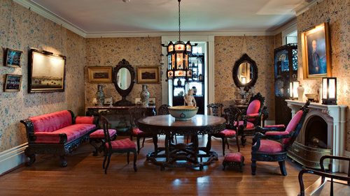 Traditional victorian-style drawing room with ornate furniture and patterned wallpaper.