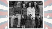 A black and white photo of a smiling family with two adults and two teens sitting on a fence, framed by a star-patterned border.