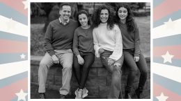 A black and white photo of a smiling family with two adults and two teens sitting on a fence, framed by a star-patterned border.