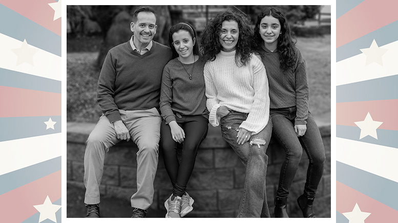 A black and white photo of a smiling family with two adults and two teens sitting on a fence, framed by a star-patterned border.