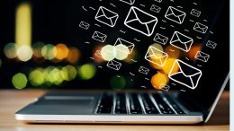 Illustrated email icons hover above a laptop keyboard, set against a vibrant backdrop of colorful lights. Discover how the Pomodoro technique can help your small business stay focused and energized in this captivating scene from Small Business Corner.