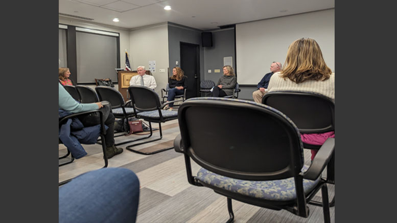 In a small conference room, people engage in a vibrant discussion, their chairs forming a circle. As the U.S. flag stands proudly by the lectern, one topic dominates: the Milton Community Resilience Building Workshop's final summary of findings report.