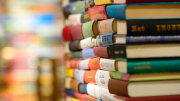 A close-up of two stacks of colorful hardcover books on a shelf, with a blurred background.