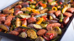 Discover a delectable tray of roasted vegetables and sausages, featuring potatoes, asparagus, bell peppers, and Brussels sprouts. Catch this delicious creation in the 2025 Cookbook Club's hot sheet at Milton Public Library on April 3!.