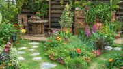 stunning gardens in a lush scene featuring a stone path, vibrant flowers, and greenery. A wooden table and chairs sit cozily in the corner, while a wooden fence entwined with climbing plants