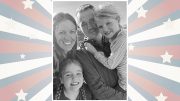 Smiling family of four, including two children, posing in front of a backdrop with red, white, and blue stars and stripes.