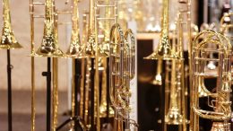 A collection of shiny brass trombones on display, standing on black stands in a well-lit room, awaiting The Boneheads Trombone Choir's performance at Milton Public Library on April 5, 2025.