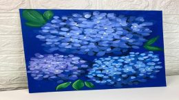 A painting featuring three clusters of blue and purple hydrangea flowers with green leaves on a dark blue background, created during a Hydrangea Art Workshop, leaning against a textured white wall.