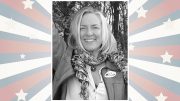 Smiling person wearing a scarf and jacket with an "I Voted" sticker, set against a starburst background with stars and stripes.
