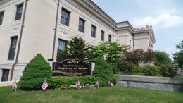 Exterior view of the Norfolk County Registry of Deeds building, with a sign and small American flags in front, surrounded by bushes and flowers—reflecting Norfolk County Real Estate activity as of April 2025.