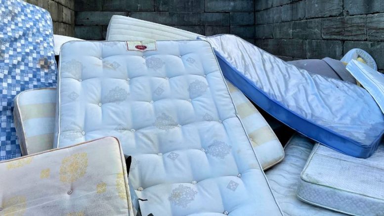 A pile of used mattresses stacked against a stone wall, showing various patterns and colors—perfect for illustrating the need for mattress disposal Milton services.