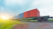 A freight train carrying shipping containers moves at speed along railroad tracks through a grassy landscape under a bright sky, highlighting the importance of avoiding common shipping container mistakes during transit.