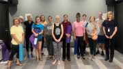 A group of people holding yoga mats stands together in a room, smiling at the camera as The Milton Public Library announces adult programs for August 2025.